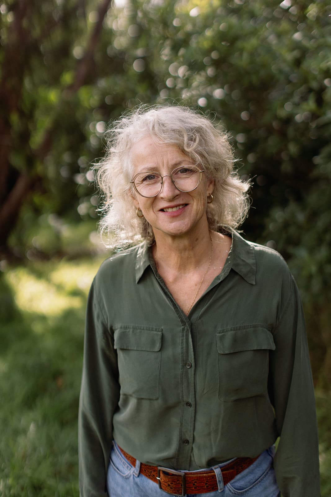 Sue Lansdown standing in dappled afternoon light among Australian native bushland, smiling gently.