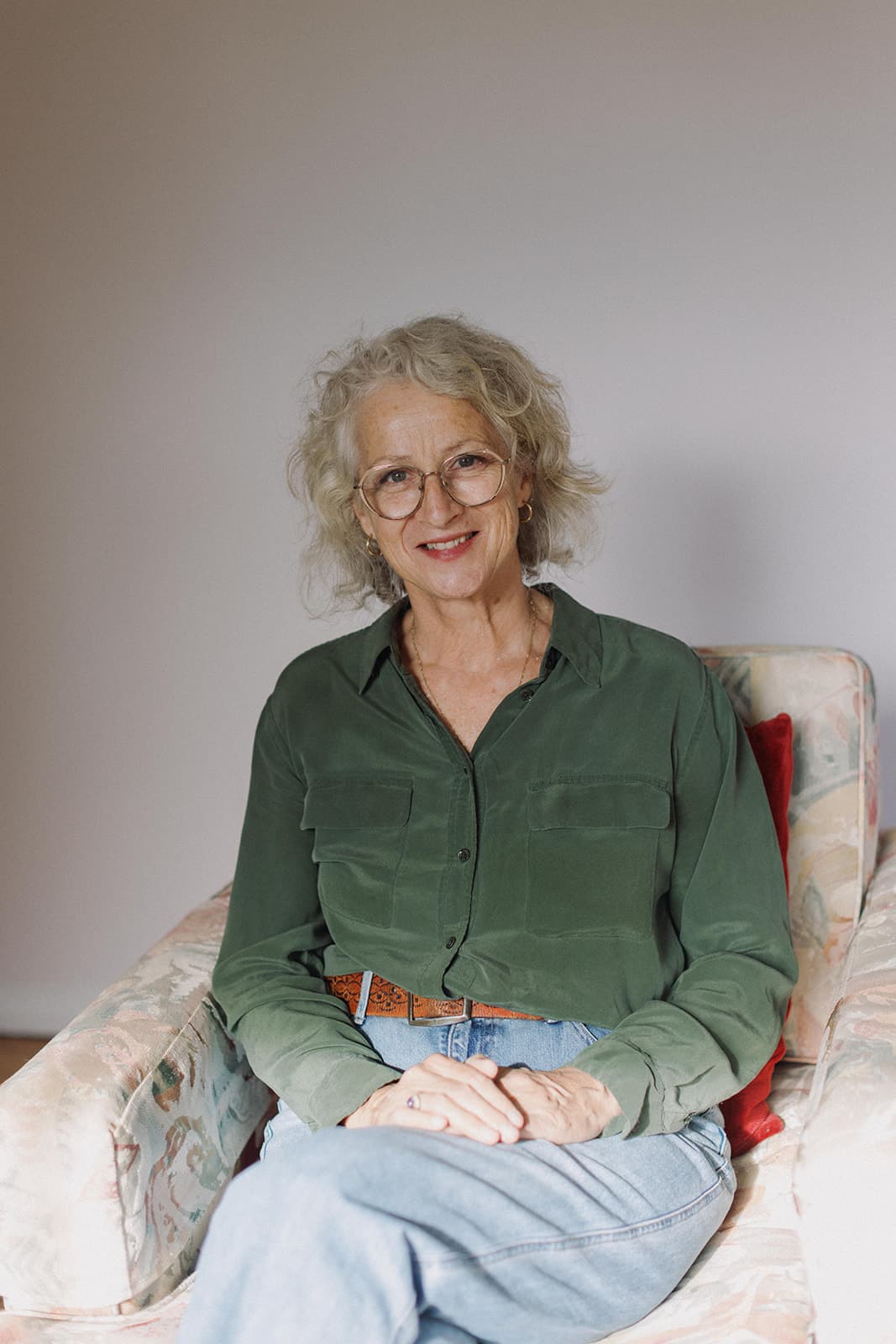Sue Lansdown sitting in a softly-lit room, hands resting in her lap, listening attentively.